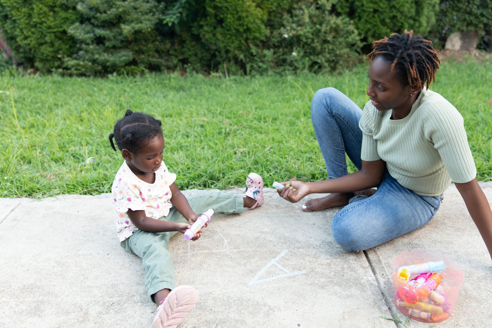 An educator drawing with chalk outdoors with a toddler