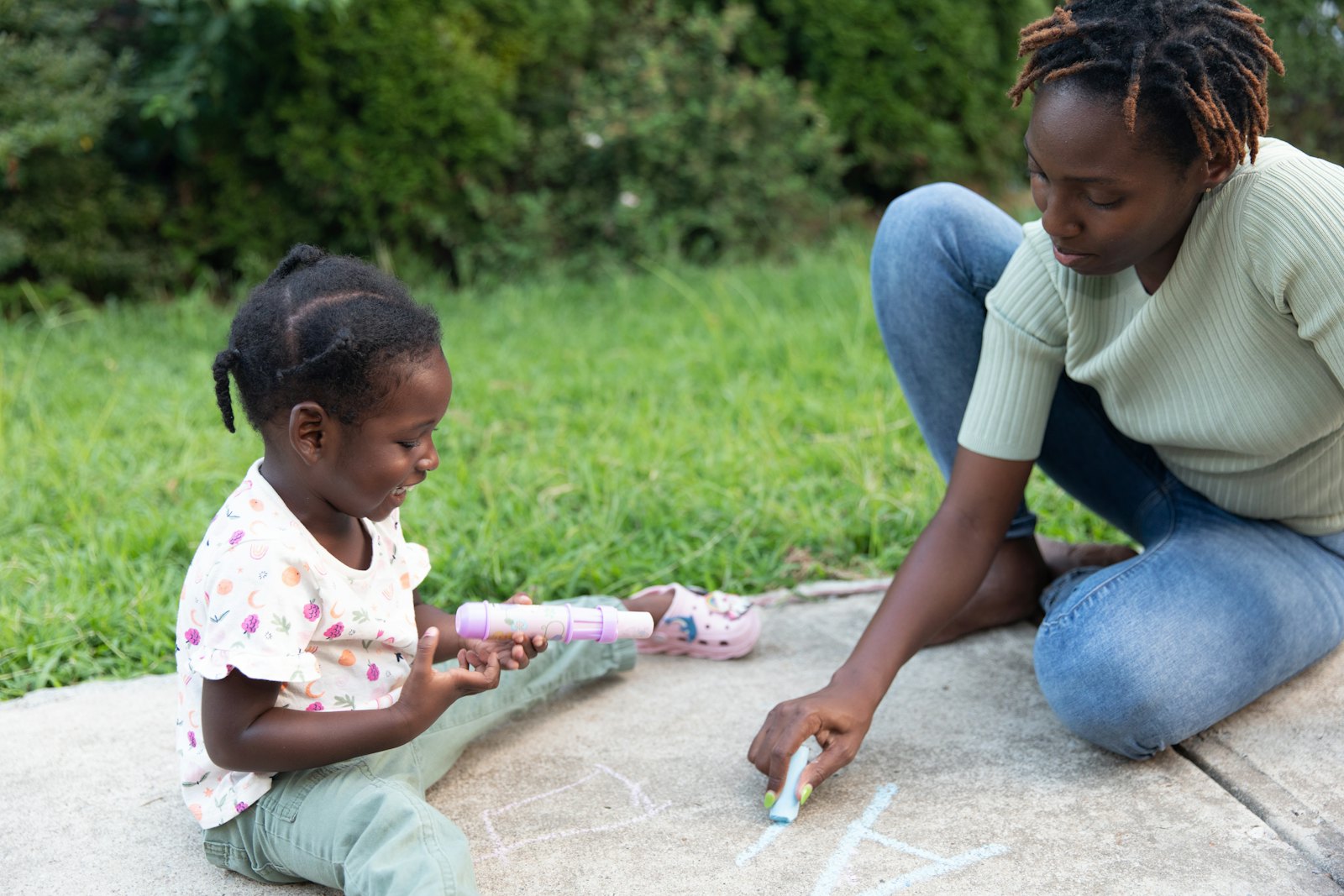 A home childcare provider drawing with chalk outside with a child